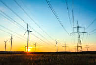 Hochspannungsleitungen mit Windkraftanlagen im Hintergrund bei Sonnenuntergang